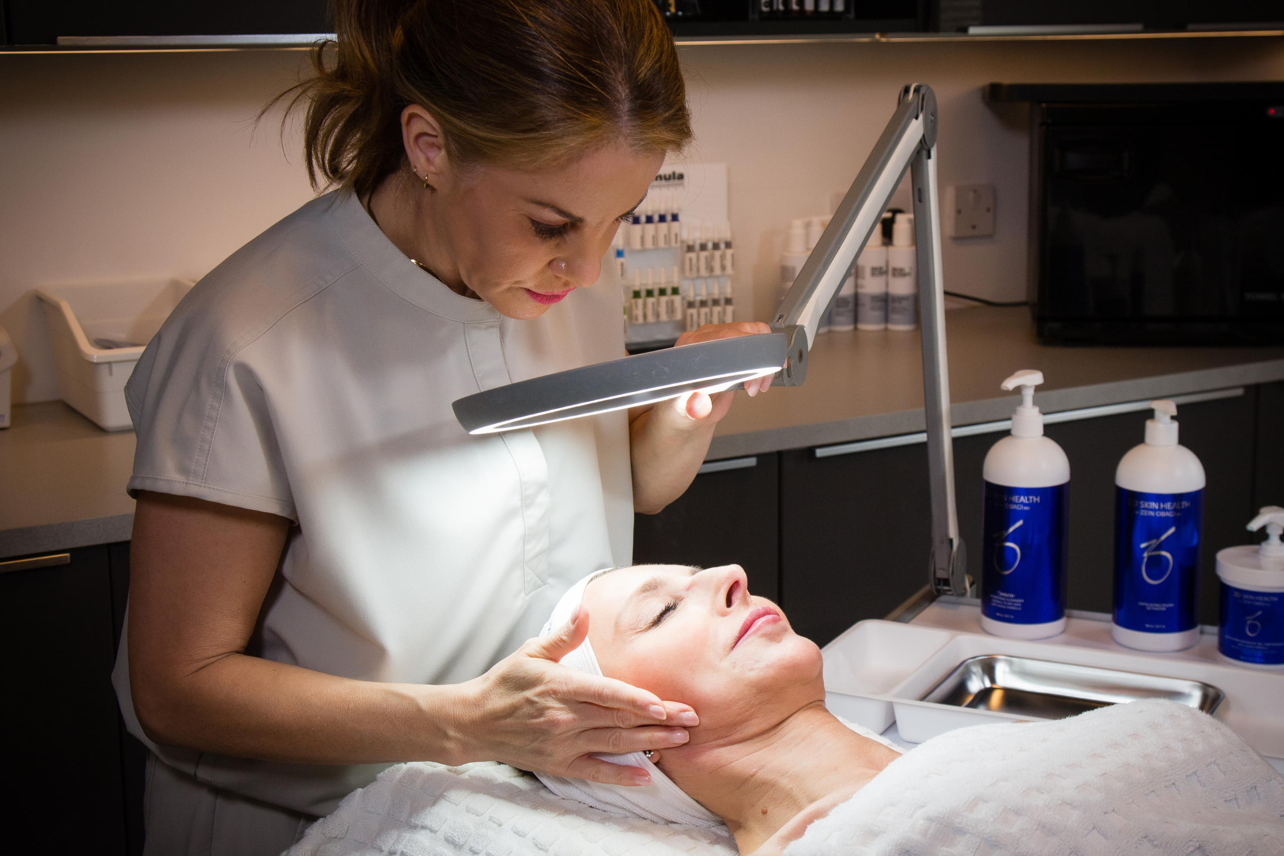 Photo of skin health aesthetician / expert administering a facial treatment to a woman on the treatment table